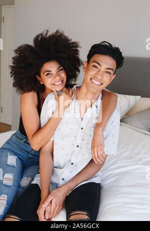 Happy young woman with arms around boyfriend while sitting on bed, portrait Stock Photo