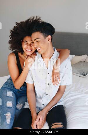 Happy young woman with arms around boyfriend while sitting on bed Stock Photo