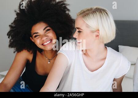 Two happy young female friends sitting on bed, portrait Stock Photo