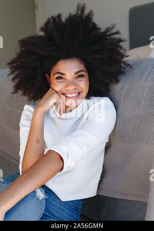 Happy young woman with afro hairstyle sitting on bedroom floor, portrait Stock Photo