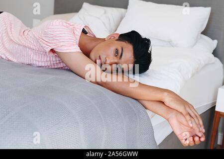 Young man lying on bed looking at camera, portrait Stock Photo