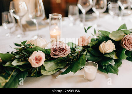 Place setting at wedding reception table with rose garland decoration, candles and drinking glasses Stock Photo