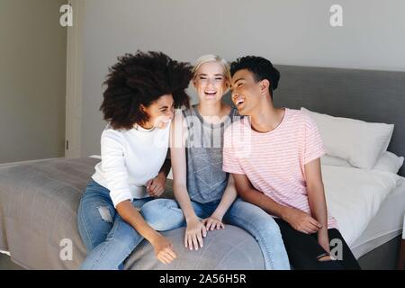 Young man and two female friends sitting on bed laughing together Stock Photo