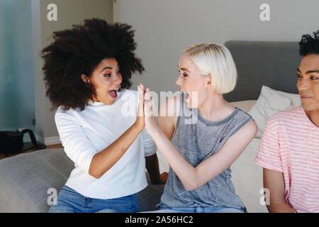 Young man and two female friends sitting on bed high fiving Stock Photo