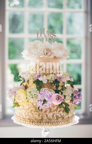 Mr and Mrs wedding cake decorated with gold patterns and icing flowers at wedding reception Stock Photo