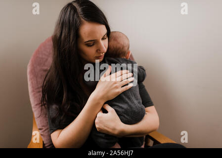 Young woman holding baby son in living room armchair Stock Photo