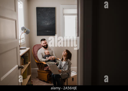 Young man with baby son on lap, laughing with daughter in living room