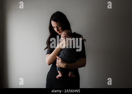 Young woman carrying baby son in arms, low key Stock Photo