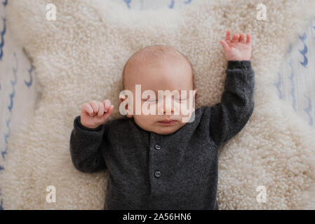 Baby boy sleeping on sheepskin rug in crib, overhead view Stock Photo