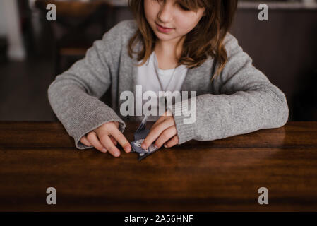 Girl at table folding paper, doing origami, head and shoulders Stock Photo