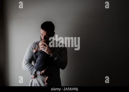 Young man carrying baby son in arms, low key Stock Photo