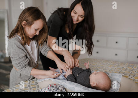 Girl helping mother change baby brother's diaper on bed