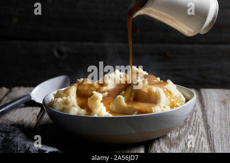 Jug of gravy being poured onto bowl of steaming mashed potatoes, studio shot Stock Photo