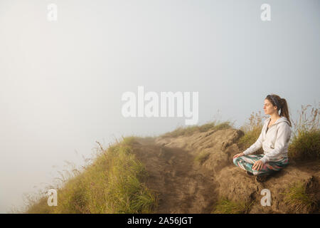 Young woman practicing yoga on top of misty mountain, Bali, Indonesia Stock Photo