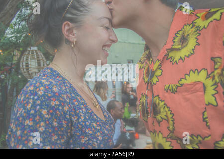 Young man giving girlfriend a kiss on the forehead at community garden party, cropped side view Stock Photo
