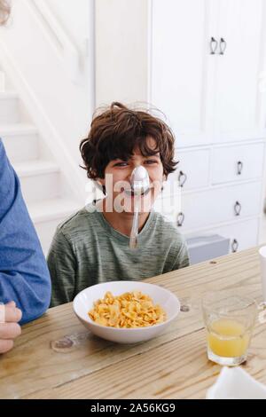 Boy laughing at spoon sticking on nose at breakfast Stock Photo