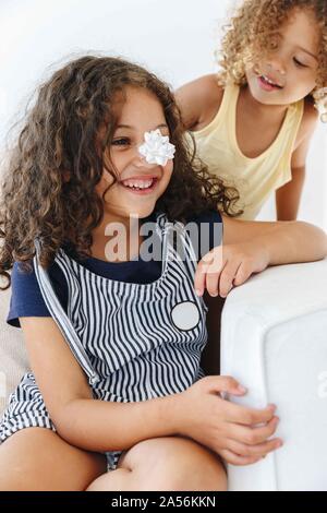 Sisters smiling over paper flower on nose Stock Photo