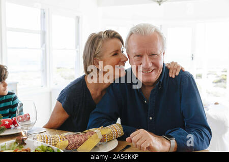 Woman whispering into smiling man's ear at home party Stock Photo