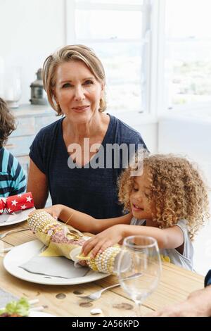 Woman with granddaughter playing with Christmas cracker at dining table Stock Photo