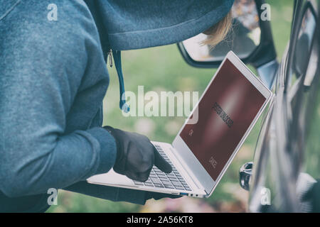 Hooded thief tries to break the car's security systems with laptop. Hacking modern car concept Stock Photo