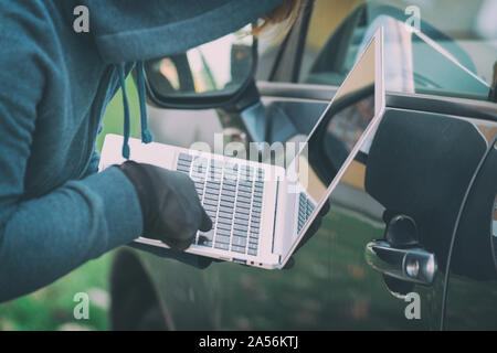 Hooded thief tries to break the car's security systems with laptop. Hacking modern car concept Stock Photo