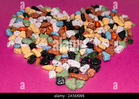 Love concept.Heart-shaped decoration from colorful pebbles on a pink background.choco rocks looks like pebbles.close up. Stock Photo