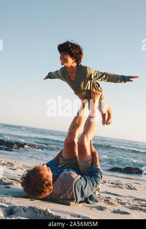 Father lifting son in mid air with legs on beach