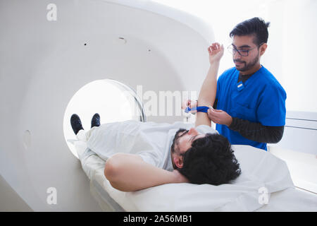 Young male radiographer preparing male patient for CT scan in radiology department Stock Photo