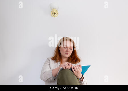 Young woman with red hair sitting and reading diary at home Stock Photo