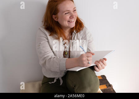 Young woman with red hair sitting holding diary and laughing Stock Photo
