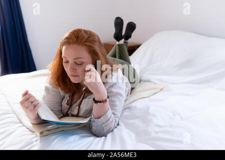 Young woman with red hair lying on bed reading her diary Stock Photo