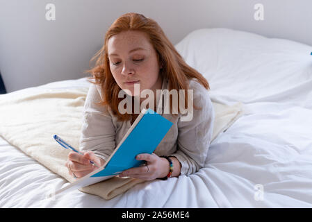 Young woman with red hair lying on bed writing in her diary Stock Photo