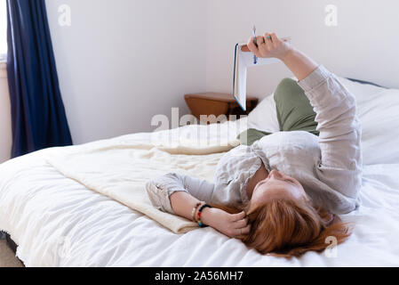 Young woman with red hair reclining on bed reading her diary Stock Photo