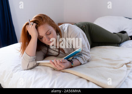Young woman with red hair lying on bed reading her diary Stock Photo