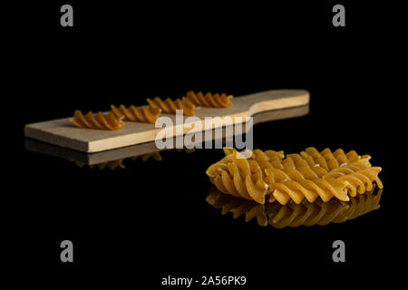 Lot of whole dry brown wholegrain fusilli on small wooden cutting board isolated on black glass Stock Photo