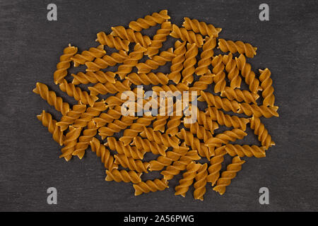 Lot of whole dry brown wholegrain fusilli flatlay on grey stone Stock Photo