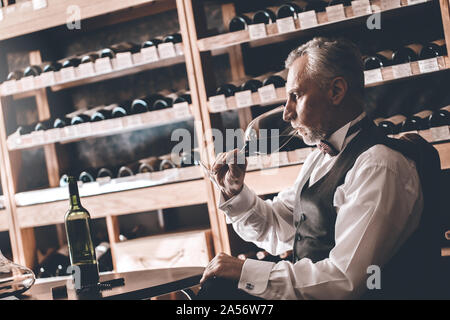 Sommelier Concept. Senior man sitting at table drinking red wine thoughtful Stock Photo