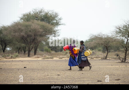 Arusha, Tanzania, 8th September 2019: maasai women walking in a savannah with a water canisters to fetch water from a well Stock Photo