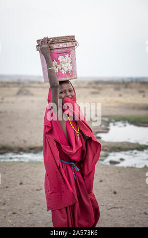 Arusha, Tanzania, 8th September 2019: maasai girl carrying a water bucket at her head Stock Photo