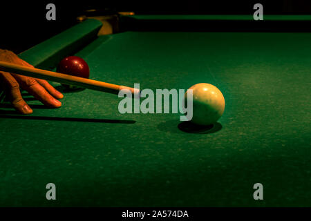 Wooden cue supported by adult male fingers while aiming at white ball on green table. Americal billiard cue sport, leisure and hobby activity. Cool va Stock Photo