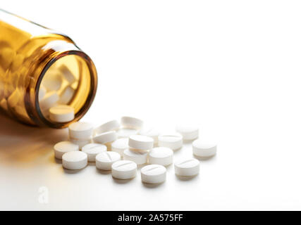 Still life with pile of white pills or tablets and glass bottle or glass and space for text. Stock Photo