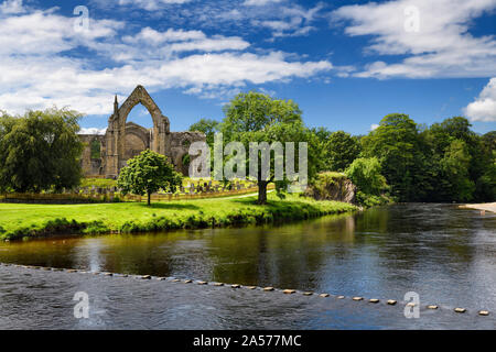 12th century Augustinian Bolton Priory church ruins on the River Wharfe with stepping stones at Bolton Abbey England Stock Photo