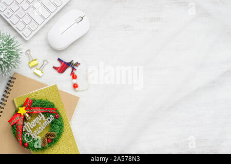 Merry Christmas sign on notebook, keyboard and mouse on nest fabric on white wooden board. Flat lay top view with copy space. Stock Photo