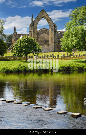 12th century Augustinian Bolton Priory church ruins with cemetery and stepping stones in River Wharfe at Bolton Abbey England Stock Photo