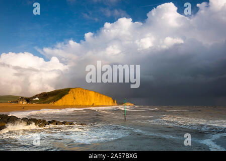 West Bay, Dorset, UK.  18th October 2019. UK Weather.  View of the East Cliff glowing a golden orange as dark stormy shower clouds clear from West Bay in Dorset after a day of sunshine and heavy showers. Picture Credit: Graham Hunt/Alamy Live News Stock Photo