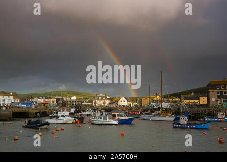 West Bay, Dorset, UK.  18th October 2019. UK Weather.  A rainbow rises above the harbour as dark stormy shower clouds clear from West Bay in Dorset after a day of sunshine and heavy showers. Picture Credit: Graham Hunt/Alamy Live News Stock Photo