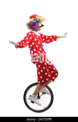 Full length profile shot of a cheerful clown riding a unicycle and making a funny grimace isolated on white background Stock Photo