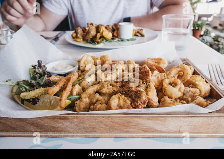 Frito misto (varied battered deep fried seafood) served on a wooden tray in a restaurant, selective focus. Stock Photo