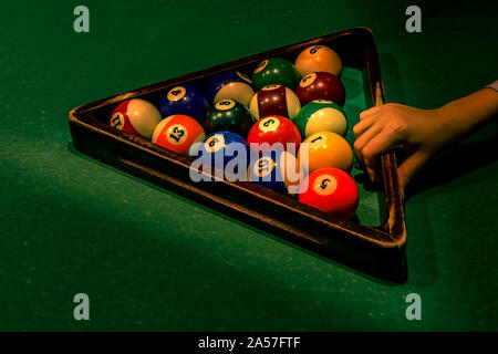 Teenager boy's hand is holding wooden triangle with set of colorful numbered balls on green table. Getting ready for Americal billiard cue sport game, Stock Photo