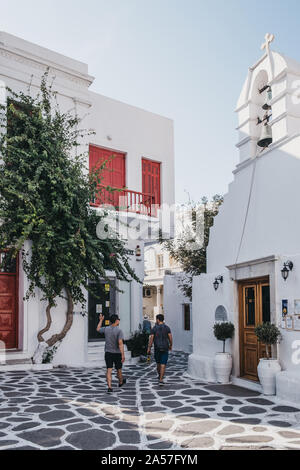 Mykonos Town, Greece - September 20, 2019: People walking past a chapel and red door building on a street in Hora (also known as Mykonos Town), the is Stock Photo